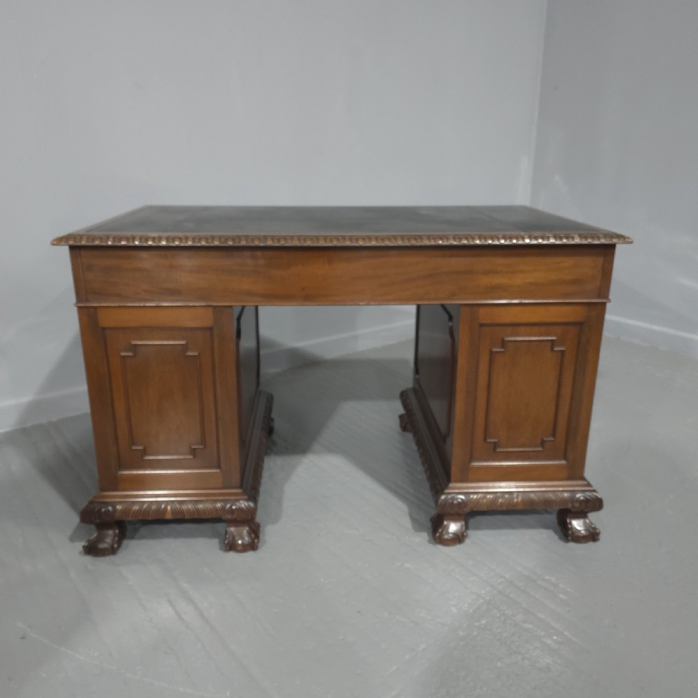 An antique mahogany pedestal desk featuring a dark leather inset surface, brass swan-neck handles, eight side drawers, a central frieze drawer, and carved claw feet. View XI