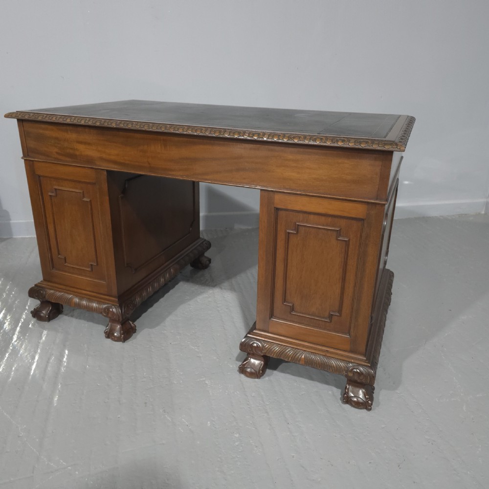 An antique mahogany pedestal desk featuring a dark leather inset surface, brass swan-neck handles, eight side drawers, a central frieze drawer, and carved claw feet. View XII