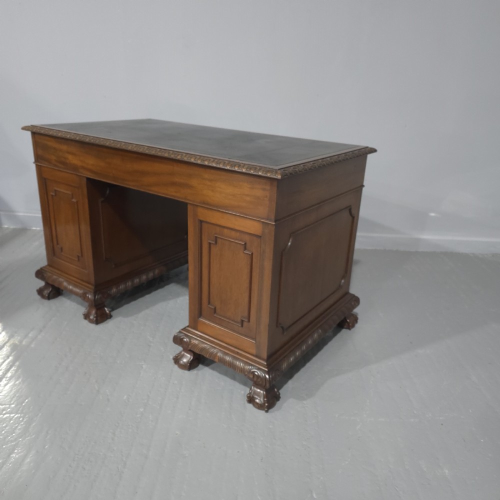 An antique mahogany pedestal desk featuring a dark leather inset surface, brass swan-neck handles, eight side drawers, a central frieze drawer, and carved claw feet. View XIII