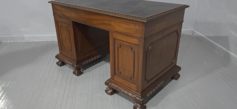 An antique mahogany pedestal desk featuring a dark leather inset surface, brass swan-neck handles, eight side drawers, a central frieze drawer, and carved claw feet. View XV