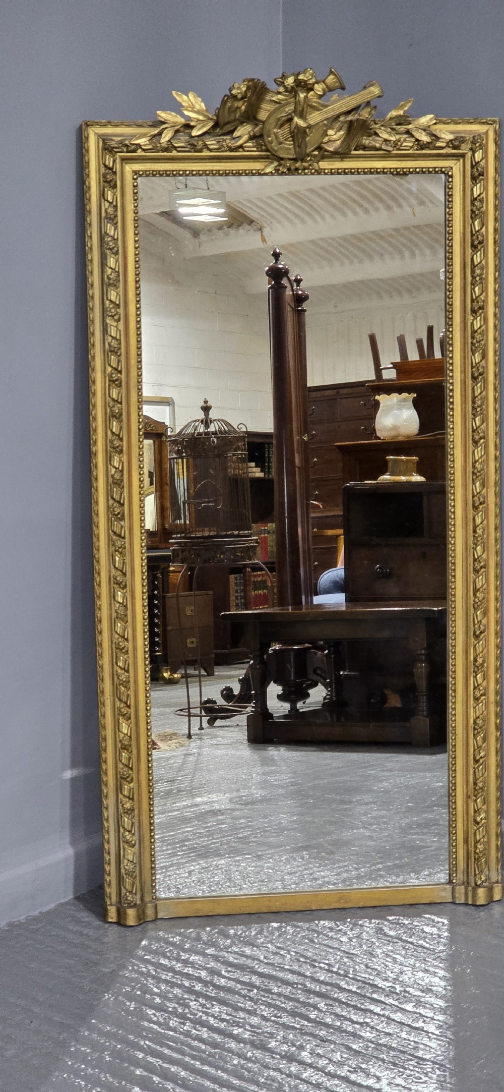 A tall rectangular French gilt mirror featuring a crest with carved musical instruments and floral frame mouldings. View II