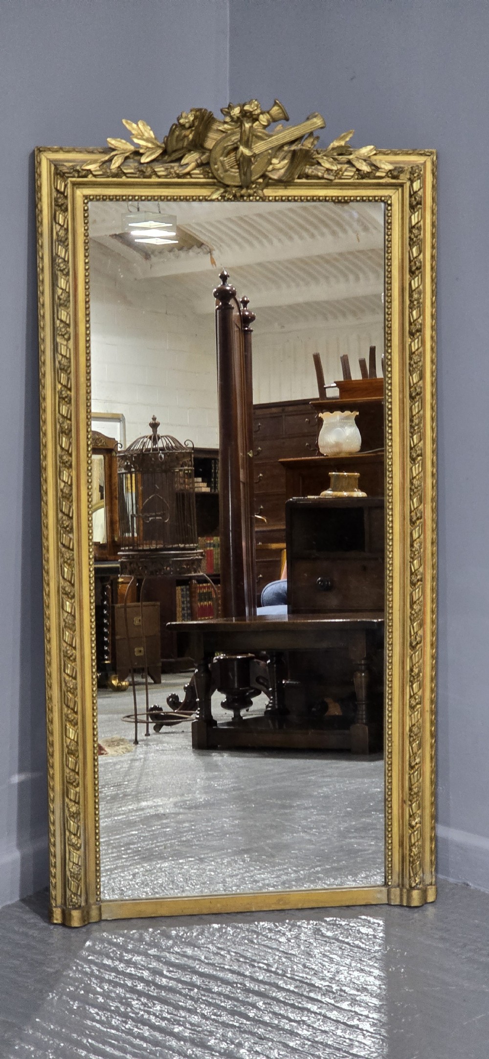 A tall rectangular French gilt mirror featuring a crest with carved musical instruments and floral frame mouldings. View III