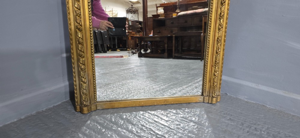 A tall rectangular French gilt mirror featuring a crest with carved musical instruments and floral frame mouldings. View IV