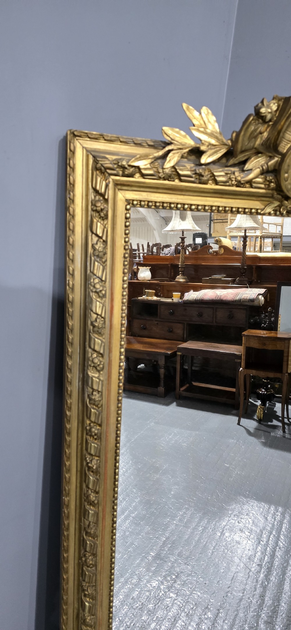 A tall rectangular French gilt mirror featuring a crest with carved musical instruments and floral frame mouldings. View VI