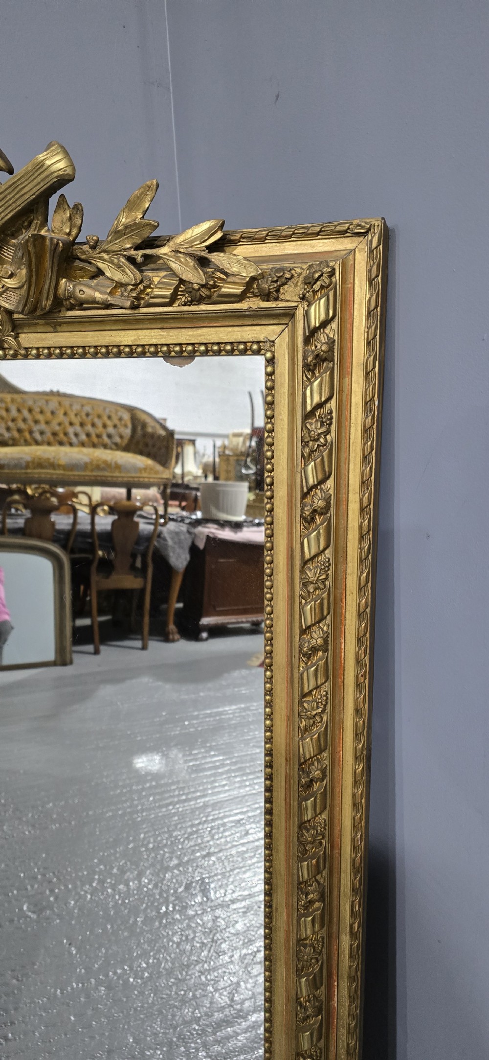 A tall rectangular French gilt mirror featuring a crest with carved musical instruments and floral frame mouldings. View VII