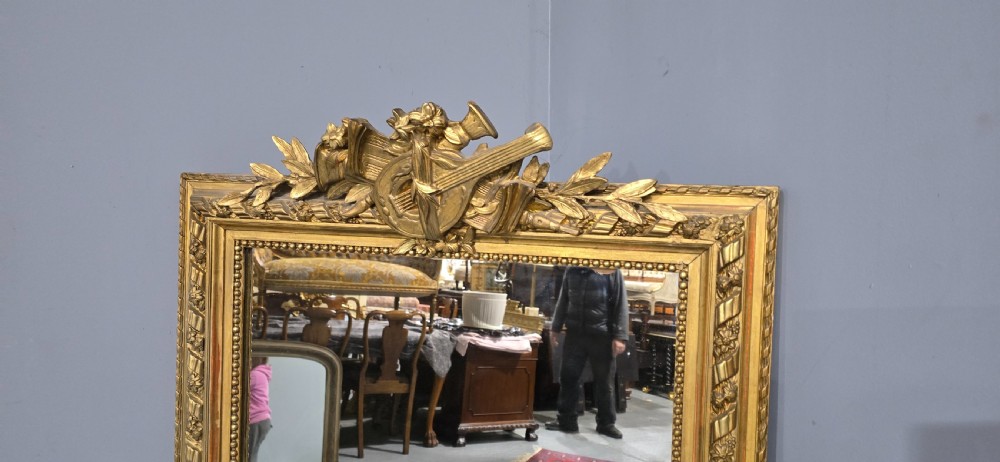 A tall rectangular French gilt mirror featuring a crest with carved musical instruments and floral frame mouldings. View VIII