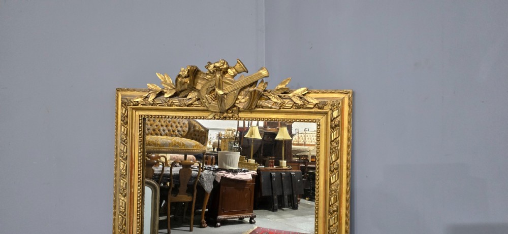 A tall rectangular French gilt mirror featuring a crest with carved musical instruments and floral frame mouldings. View IX