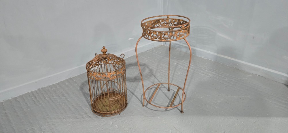 A Victorian cast iron birdcage featuring a domed roof and decorative filigree band, supported on a tall slender metal floor stand with an oxidised rust finish. View IV