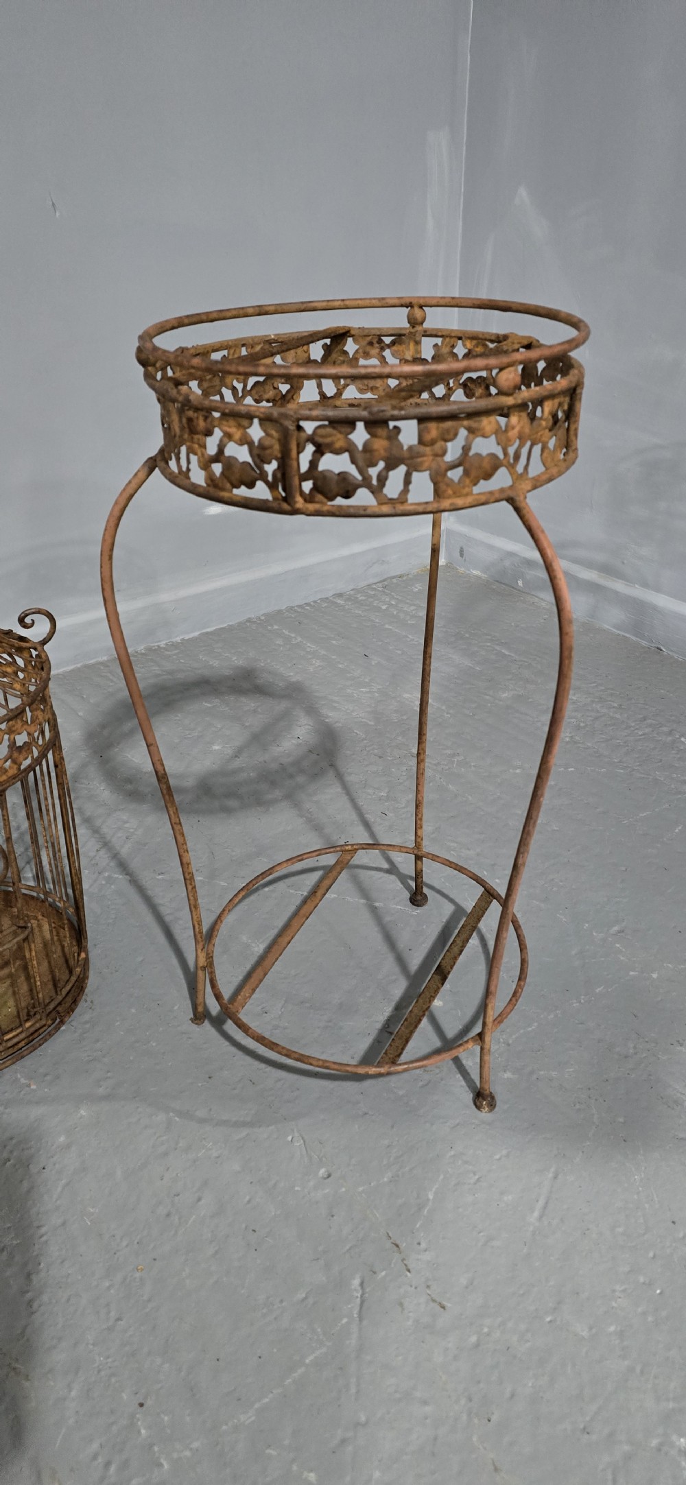 A Victorian cast iron birdcage featuring a domed roof and decorative filigree band, supported on a tall slender metal floor stand with an oxidised rust finish. View V