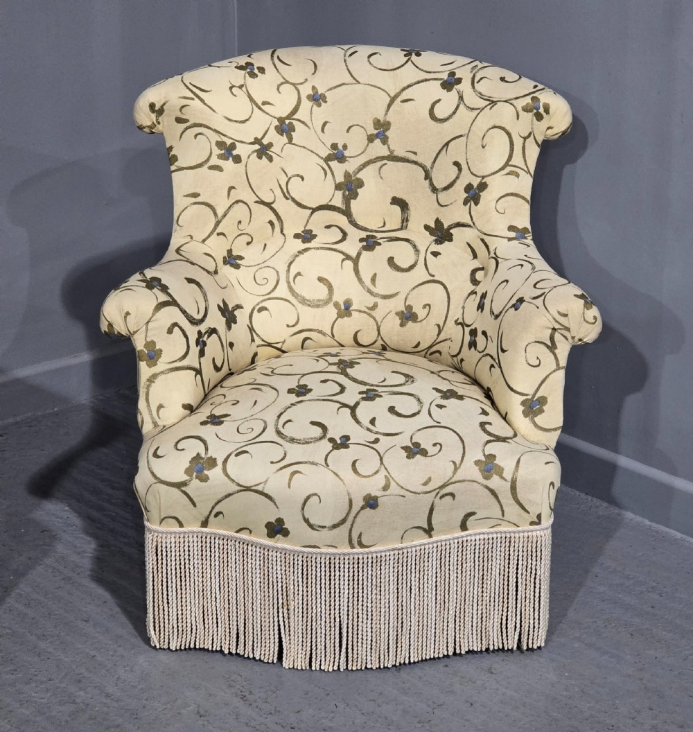 A pair of fully upholstered French Empire style armchairs covered in cream fabric with a green scroll pattern and deep tassel fringe skirting. View II