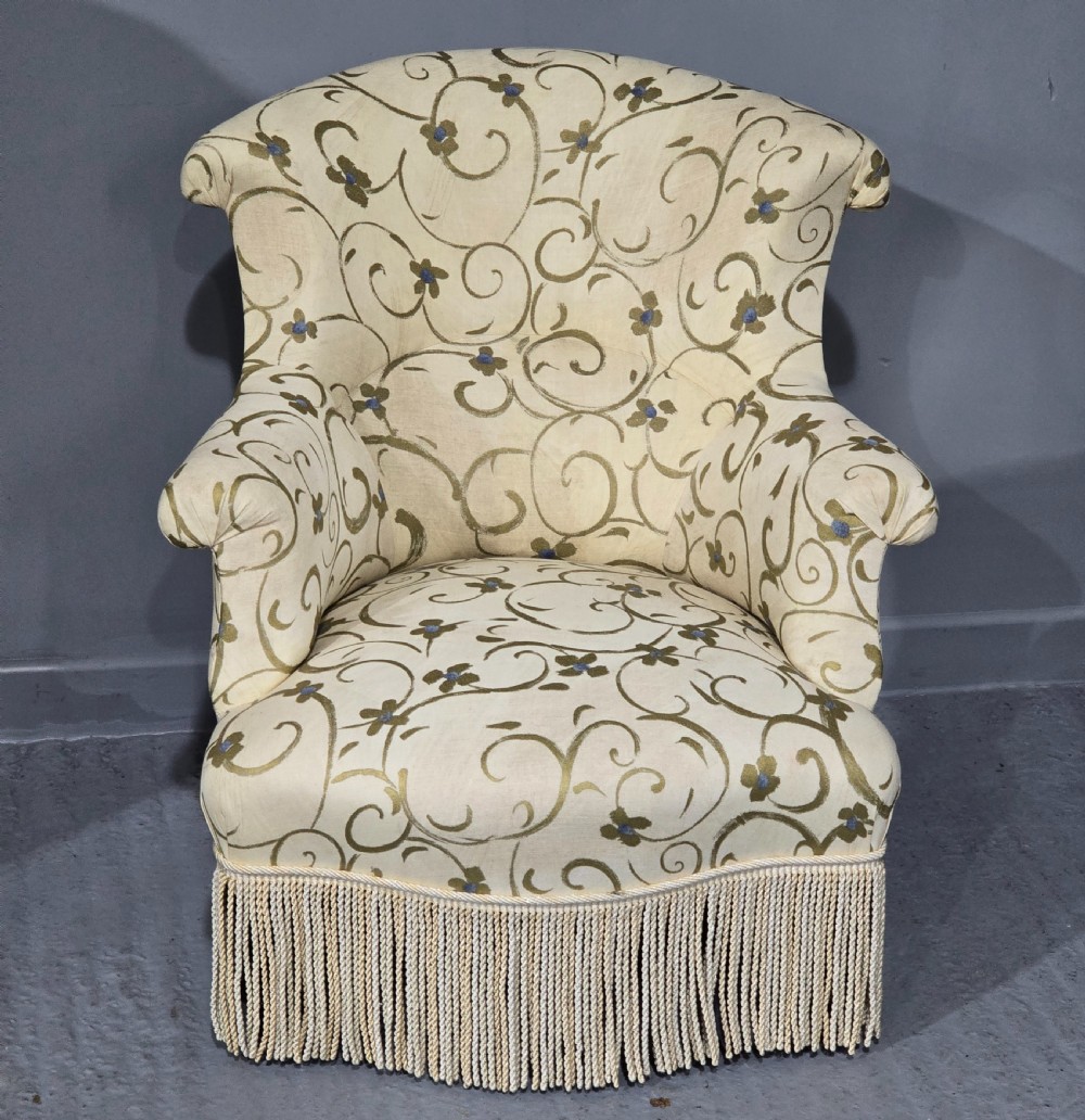 A pair of fully upholstered French Empire style armchairs covered in cream fabric with a green scroll pattern and deep tassel fringe skirting. View III