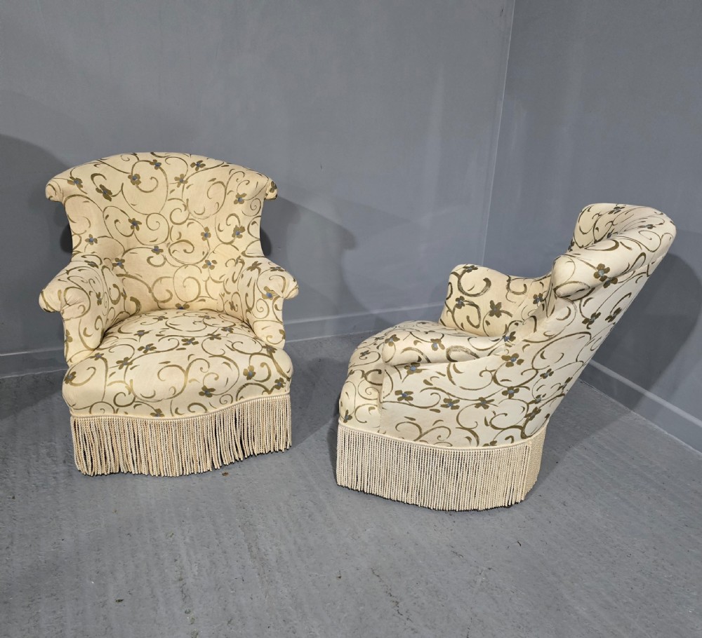 A pair of fully upholstered French Empire style armchairs covered in cream fabric with a green scroll pattern and deep tassel fringe skirting. View IV