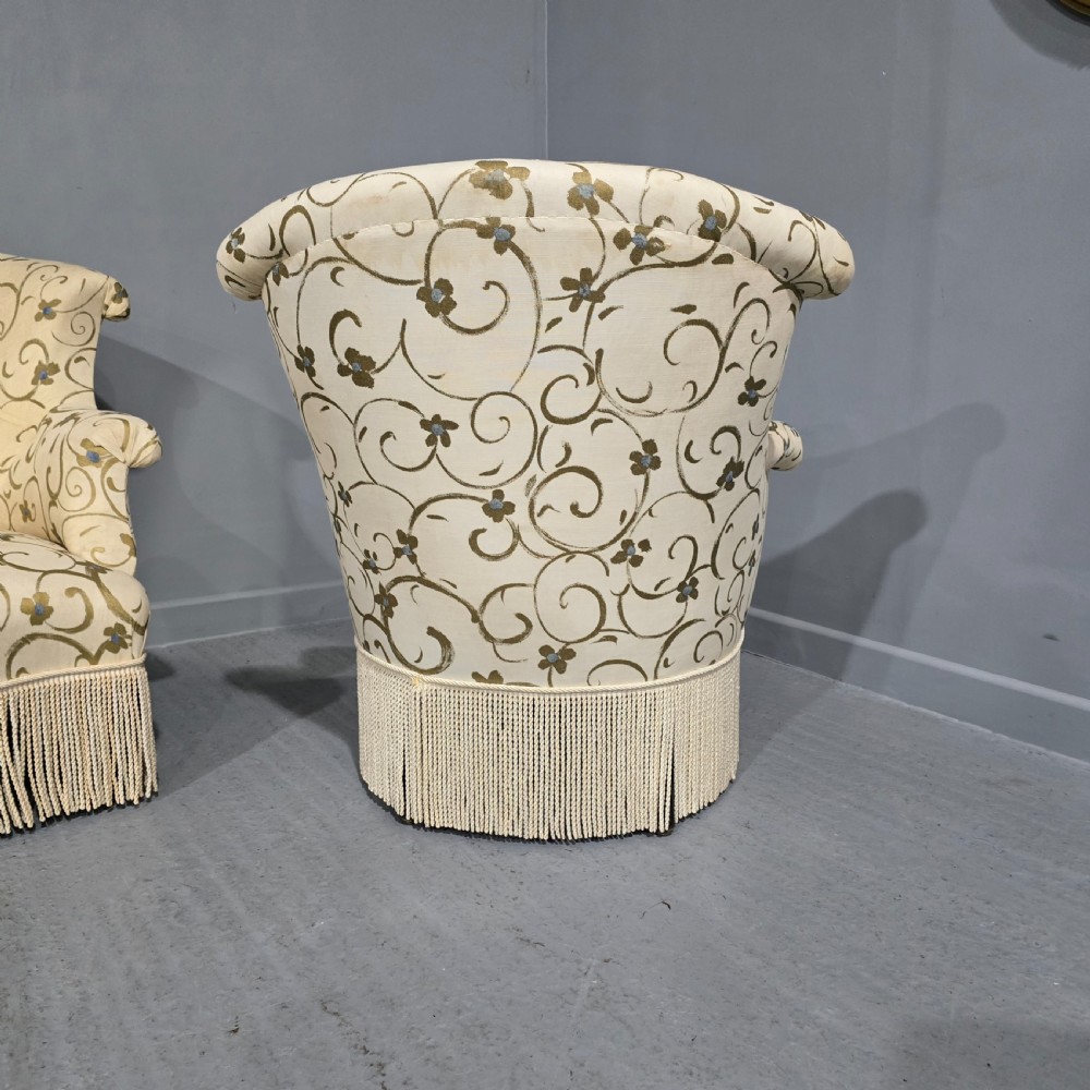 A pair of fully upholstered French Empire style armchairs covered in cream fabric with a green scroll pattern and deep tassel fringe skirting. View V