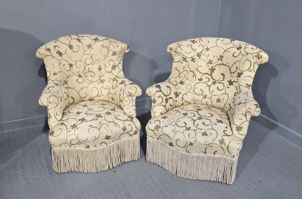 A pair of fully upholstered French Empire style armchairs covered in cream fabric with a green scroll pattern and deep tassel fringe skirting. View VII
