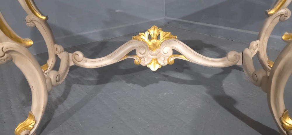A French Rococo style console table featuring off-white painted wood, carved parcel-gilt details, cabriole legs, and a shaped stretcher base. View VIII