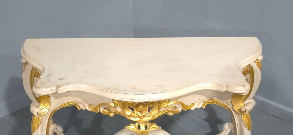 A French Rococo style console table featuring off-white painted wood, carved parcel-gilt details, cabriole legs, and a shaped stretcher base. View XI