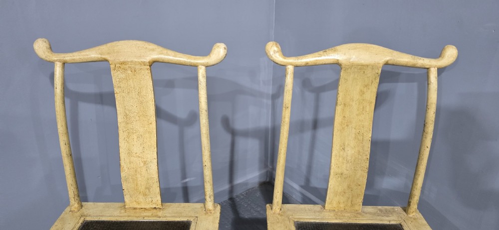 A pair of cream lacquered Chinese hall chairs featuring curved yoke crest rails, shaped splats, carved aprons, and dark inset seats. View IV