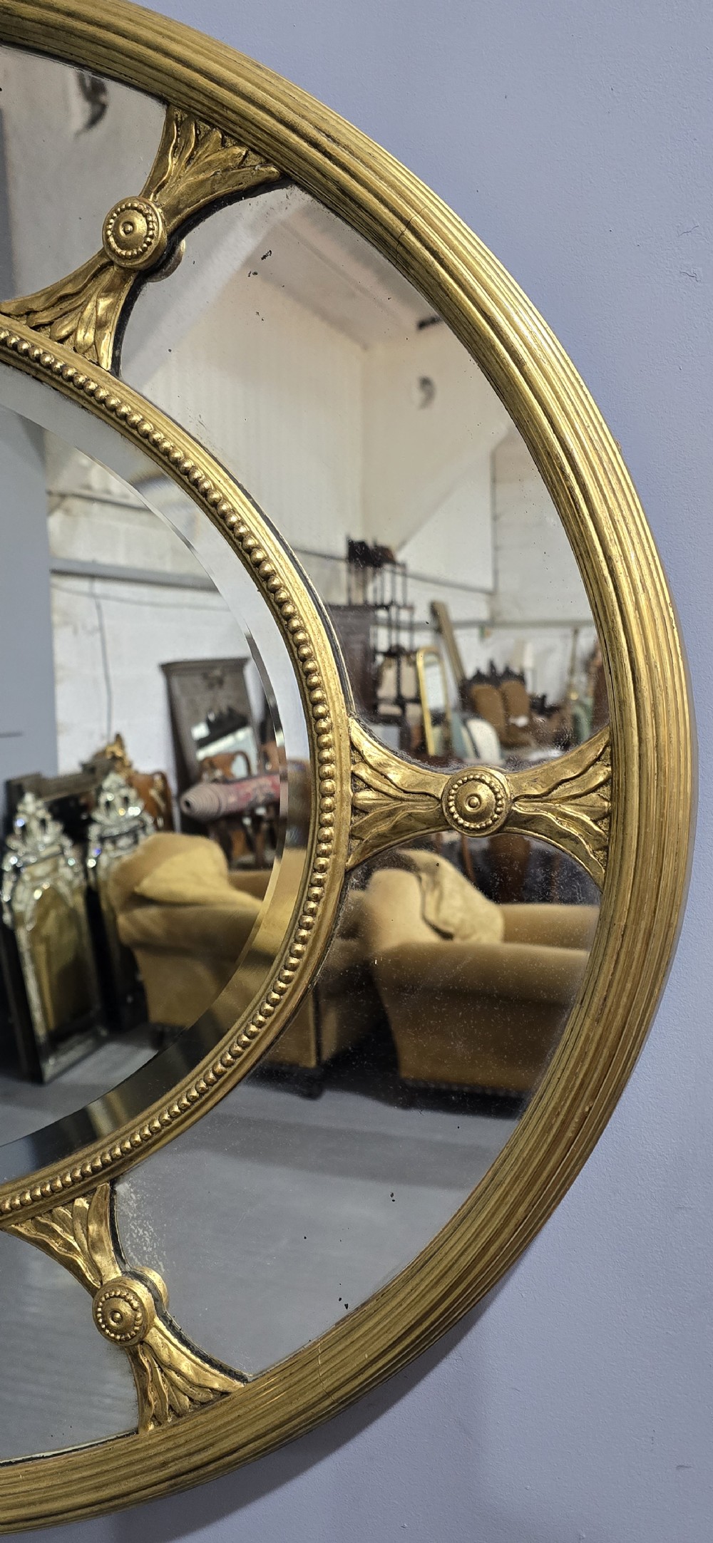 A large oval wall mirror with a beaded gold giltwood frame surrounding a central glass plate and outer sectional glass border. View III
