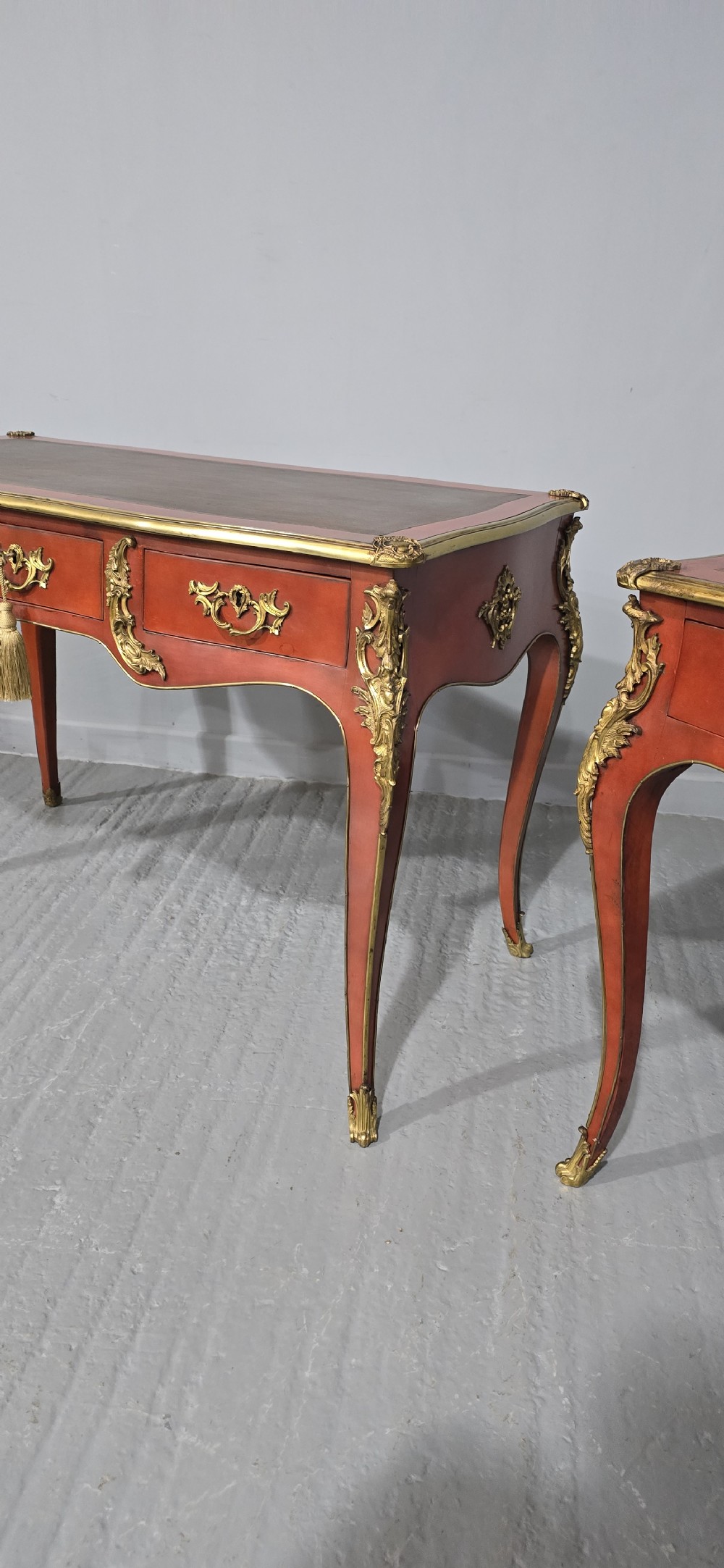 A pair of red lacquered French bureau plat writing desks featuring inset leather tops, three frieze drawers, and gilt bronze mounts on cabriole legs. View V