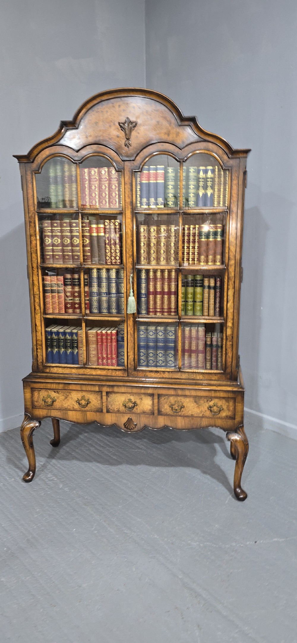 A double-door glazed burr walnut bookcase on stand featuring an arched pediment, astragal glazing bars, three lower drawers, and cabriole legs. View III