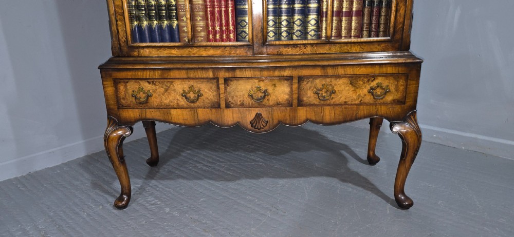 A double-door glazed burr walnut bookcase on stand featuring an arched pediment, astragal glazing bars, three lower drawers, and cabriole legs. View V