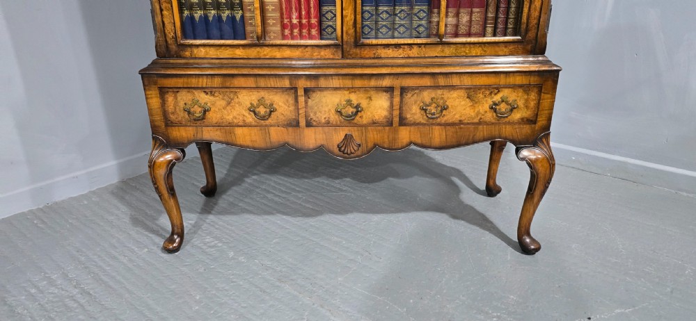 A double-door glazed burr walnut bookcase on stand featuring an arched pediment, astragal glazing bars, three lower drawers, and cabriole legs. View VI