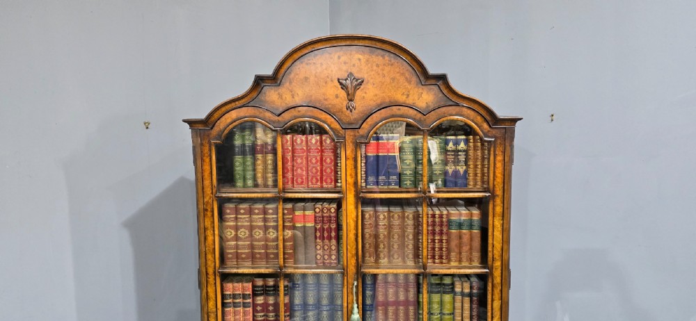 A double-door glazed burr walnut bookcase on stand featuring an arched pediment, astragal glazing bars, three lower drawers, and cabriole legs. View VII