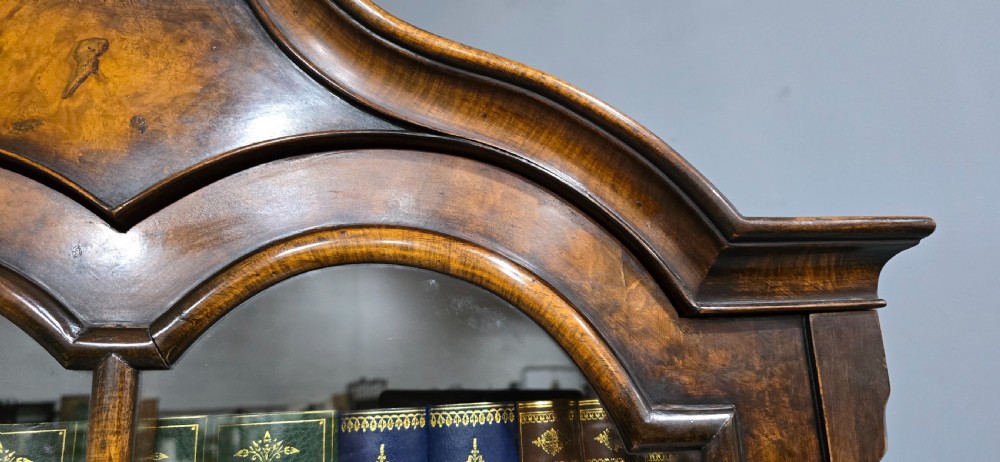 A double-door glazed burr walnut bookcase on stand featuring an arched pediment, astragal glazing bars, three lower drawers, and cabriole legs. View VIII