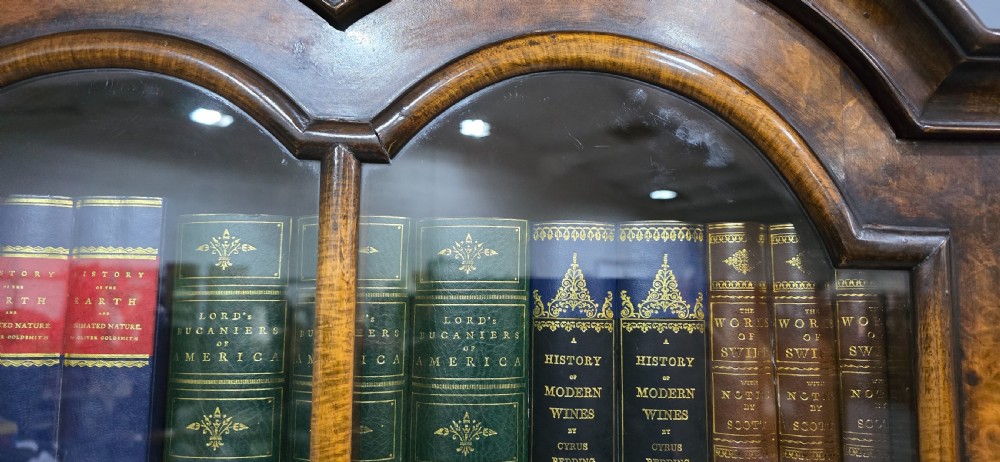 A double-door glazed burr walnut bookcase on stand featuring an arched pediment, astragal glazing bars, three lower drawers, and cabriole legs. View X