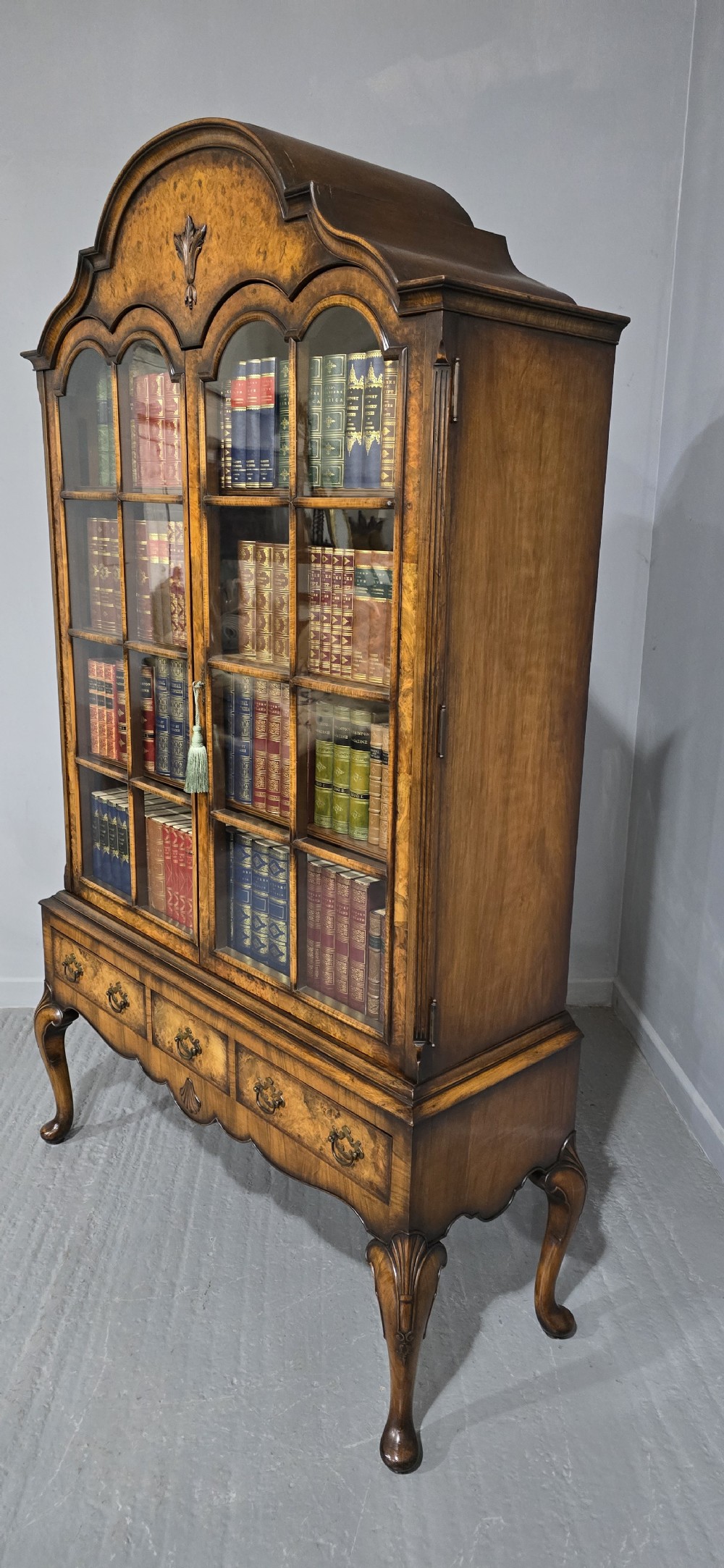 A double-door glazed burr walnut bookcase on stand featuring an arched pediment, astragal glazing bars, three lower drawers, and cabriole legs. View XII
