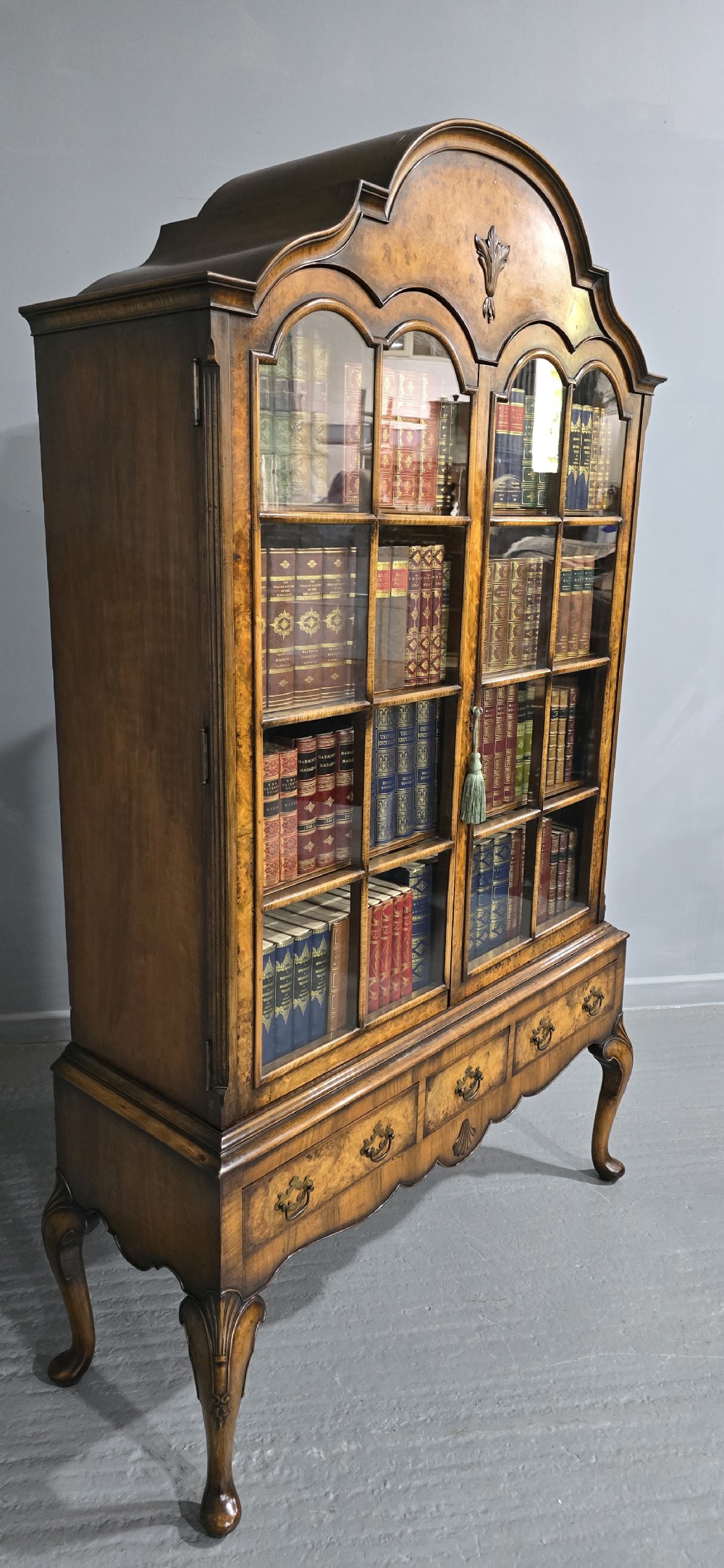 A double-door glazed burr walnut bookcase on stand featuring an arched pediment, astragal glazing bars, three lower drawers, and cabriole legs. View XIII
