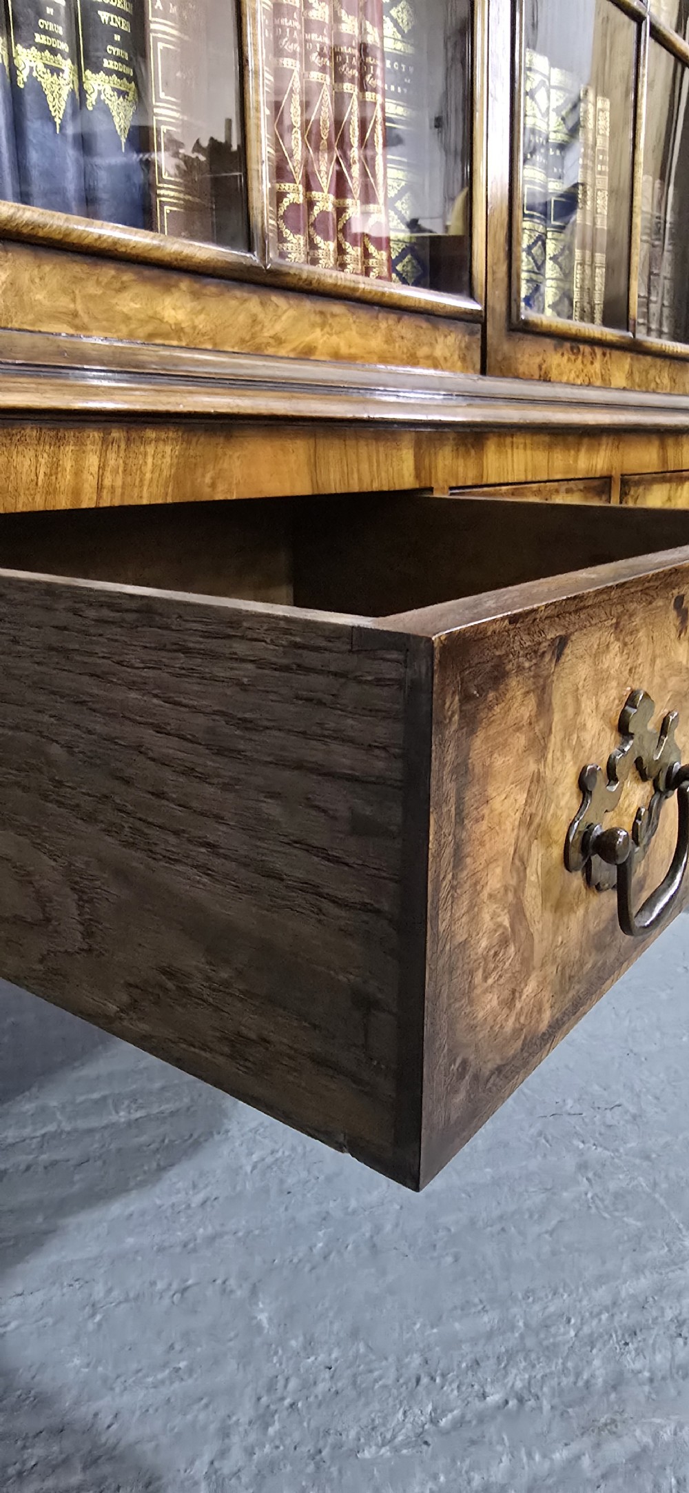 A double-door glazed burr walnut bookcase on stand featuring an arched pediment, astragal glazing bars, three lower drawers, and cabriole legs. View XIV