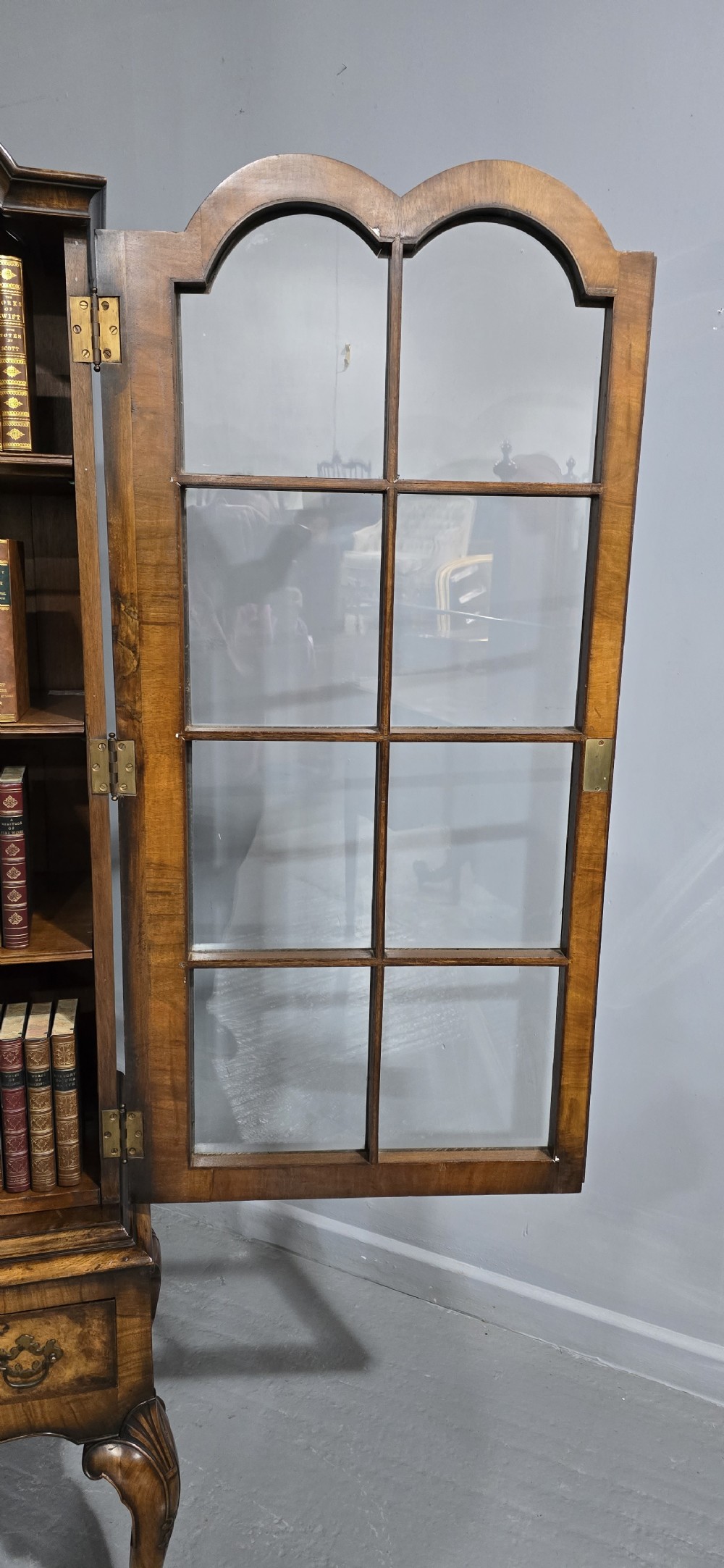 A double-door glazed burr walnut bookcase on stand featuring an arched pediment, astragal glazing bars, three lower drawers, and cabriole legs. View XVI