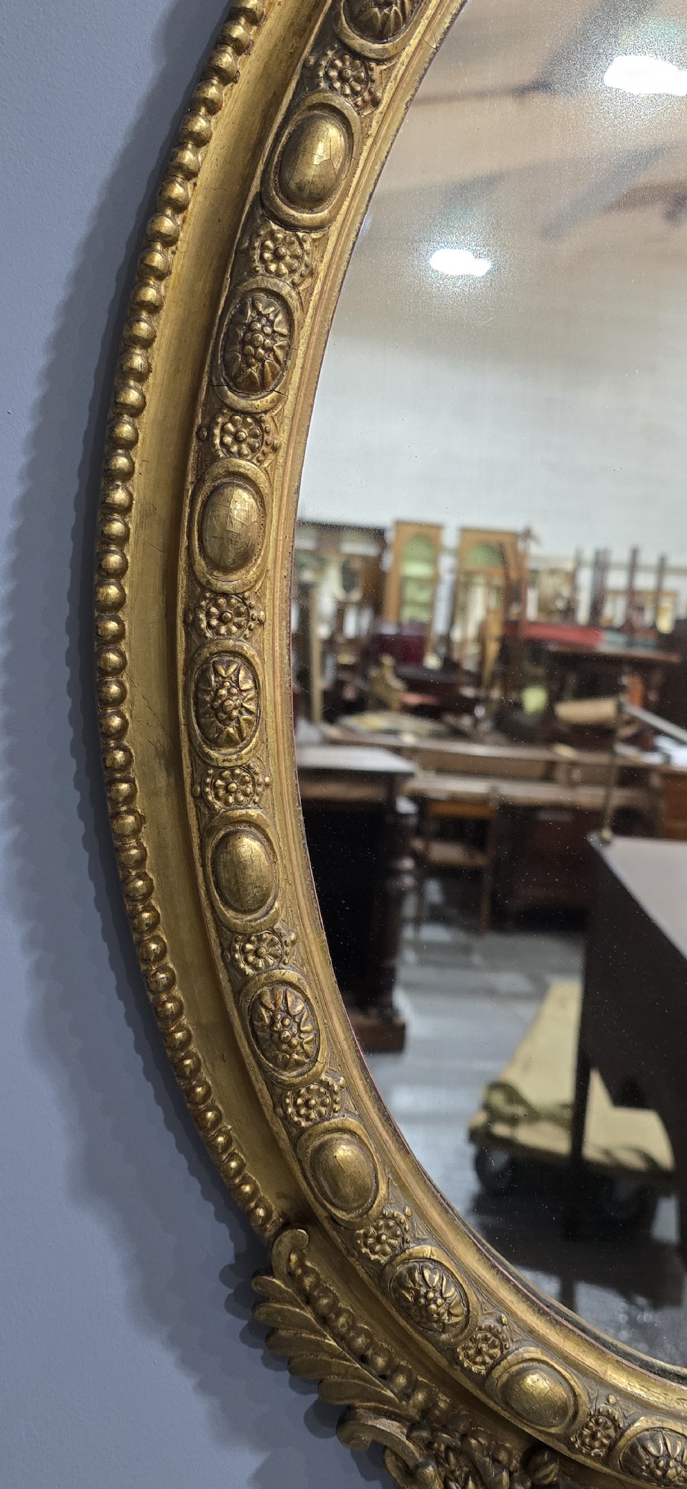 An oval giltwood wall mirror featuring an ornate carved crest with lattice detail, a beaded inner border, and a decorative bottom pendant. View VII