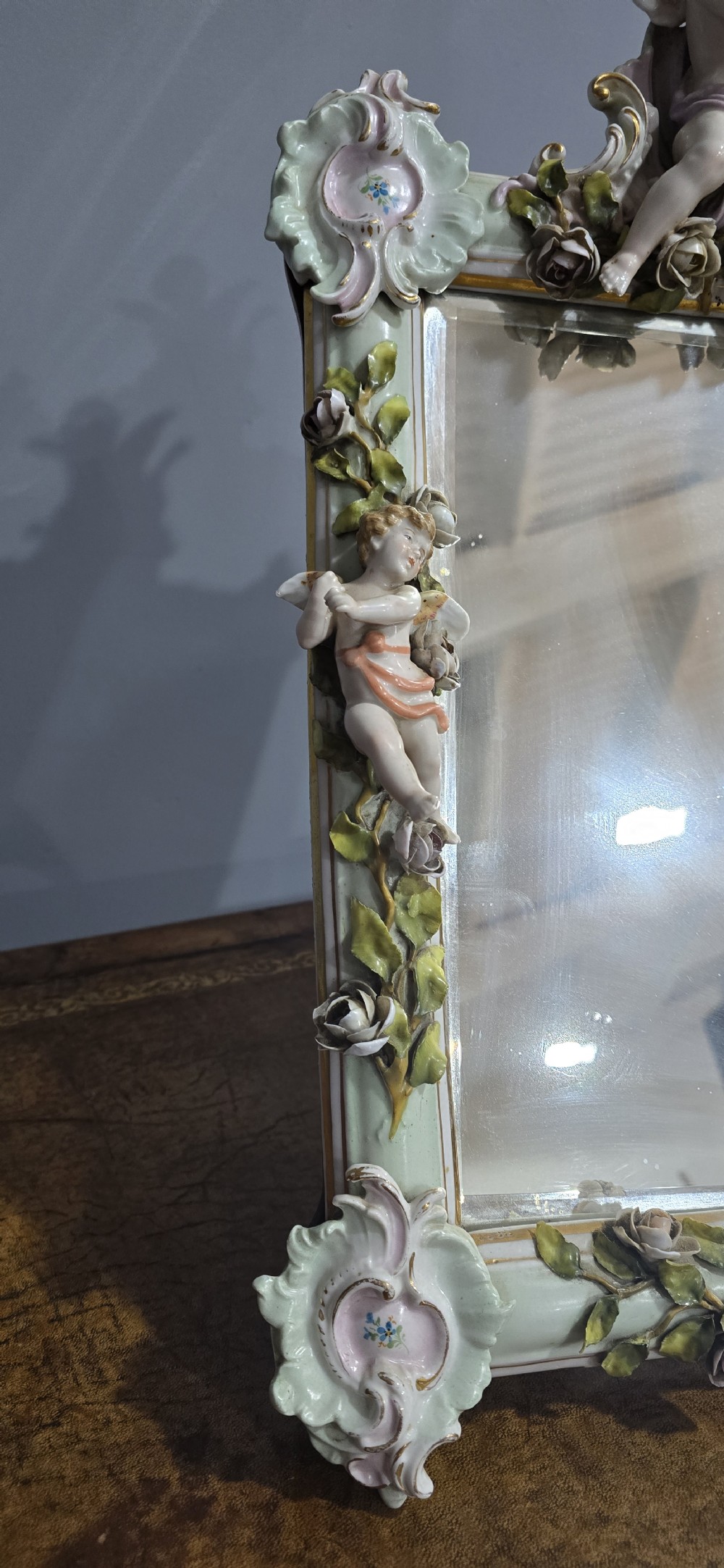 An antique Dresden porcelain easel mirror decorated with sculpted cherubs, encrusted pastel flowers, and Rococo scrollwork around a rectangular glass frame. View III