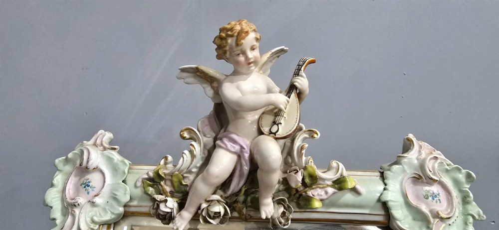 An antique Dresden porcelain easel mirror decorated with sculpted cherubs, encrusted pastel flowers, and Rococo scrollwork around a rectangular glass frame. View VII