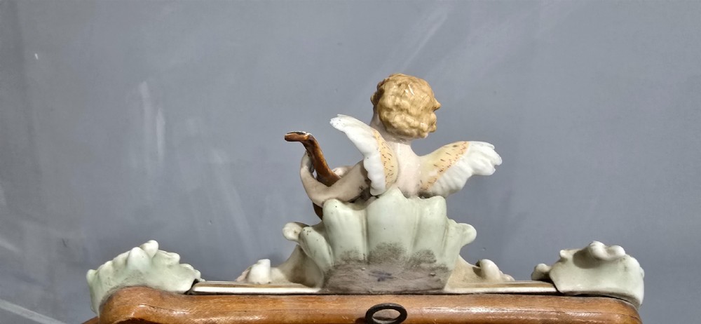 An antique Dresden porcelain easel mirror decorated with sculpted cherubs, encrusted pastel flowers, and Rococo scrollwork around a rectangular glass frame. View X