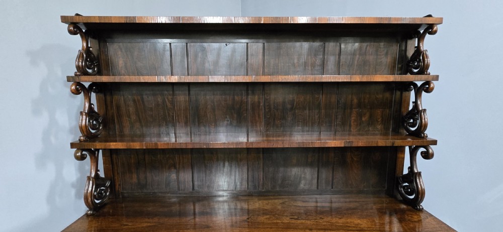 A large 19th-century William IV open mahogany waterfall bookcase with tiered graduated shelves filled with books and carved pilasters. View XII
