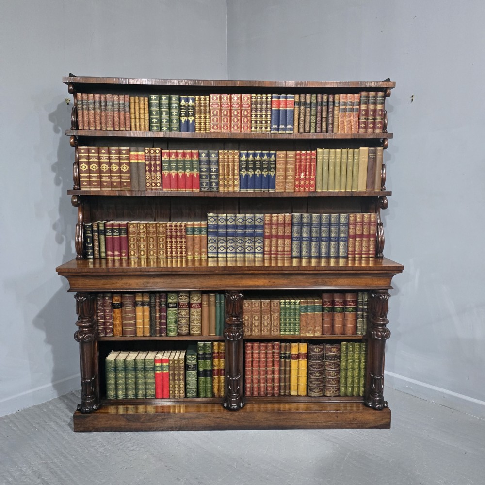 A large 19th-century William IV open mahogany waterfall bookcase with tiered graduated shelves filled with books and carved pilasters.