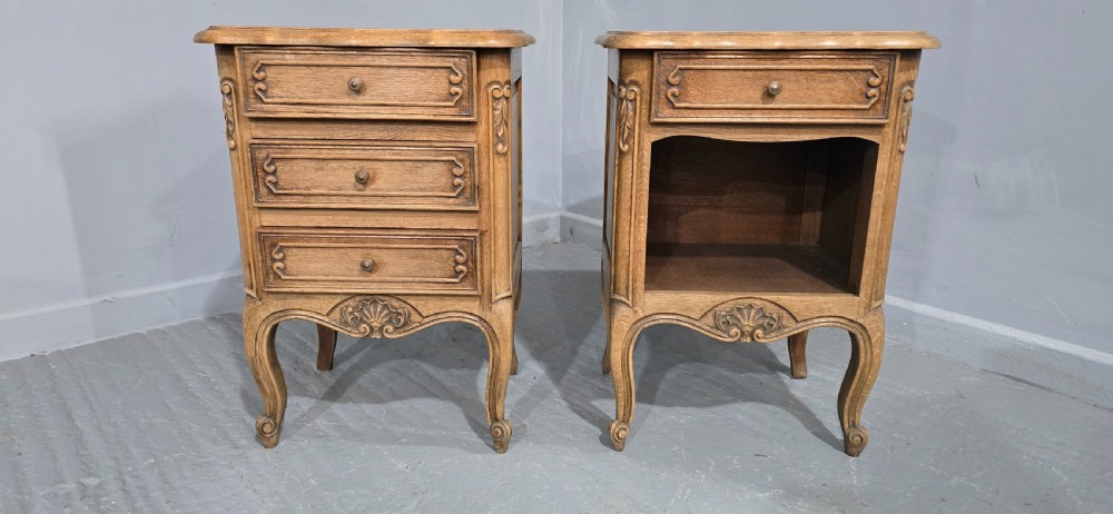 A pair of French bleached oak bedside cabinets featuring cabriole legs, carved aprons, and moulded drawer fronts, with one unit containing three drawers and the other featuring a single drawer above an open shelf. View II