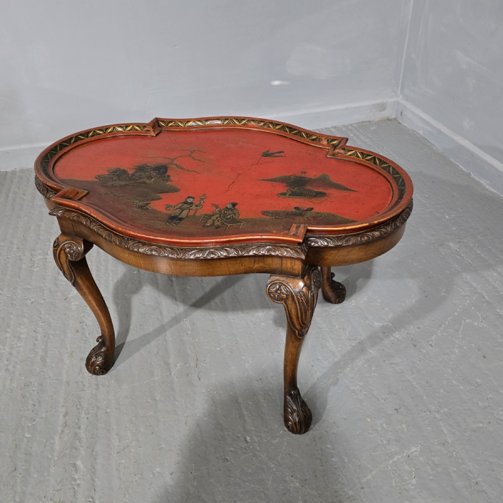 A low shaped coffee table featuring a red lacquered Chinoiserie top with painted figures and a carved walnut base with cabriole legs.