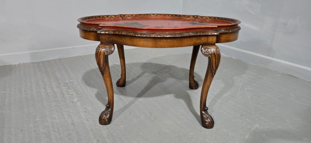 A low shaped coffee table featuring a red lacquered Chinoiserie top with painted figures and a carved walnut base with cabriole legs. View II