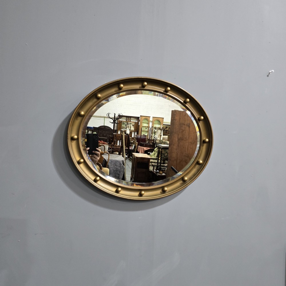 An oval Victorian gilt wall mirror featuring a molded gold frame accented with spherule ball details around the perimeter.