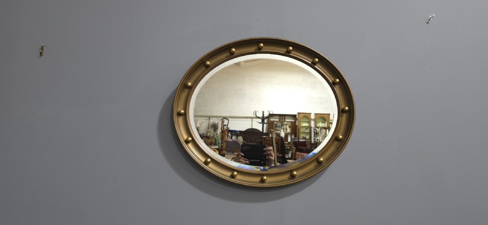 An oval Victorian gilt wall mirror featuring a molded gold frame accented with spherule ball details around the perimeter. View V