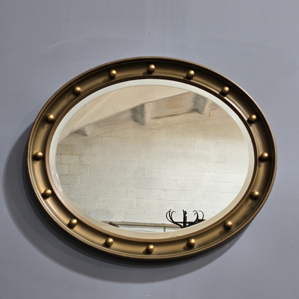 An oval Victorian gilt wall mirror featuring a molded gold frame accented with spherule ball details around the perimeter. View VI