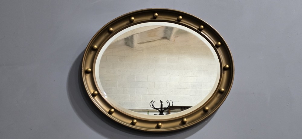 An oval Victorian gilt wall mirror featuring a molded gold frame accented with spherule ball details around the perimeter. View VIII