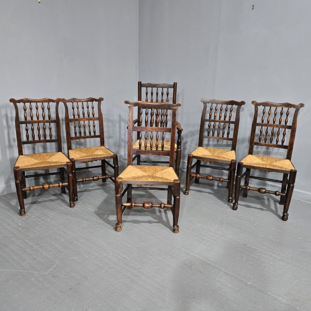 A set of six dark brown 19th-century country dining chairs featuring spindle backrests and woven rush seats.