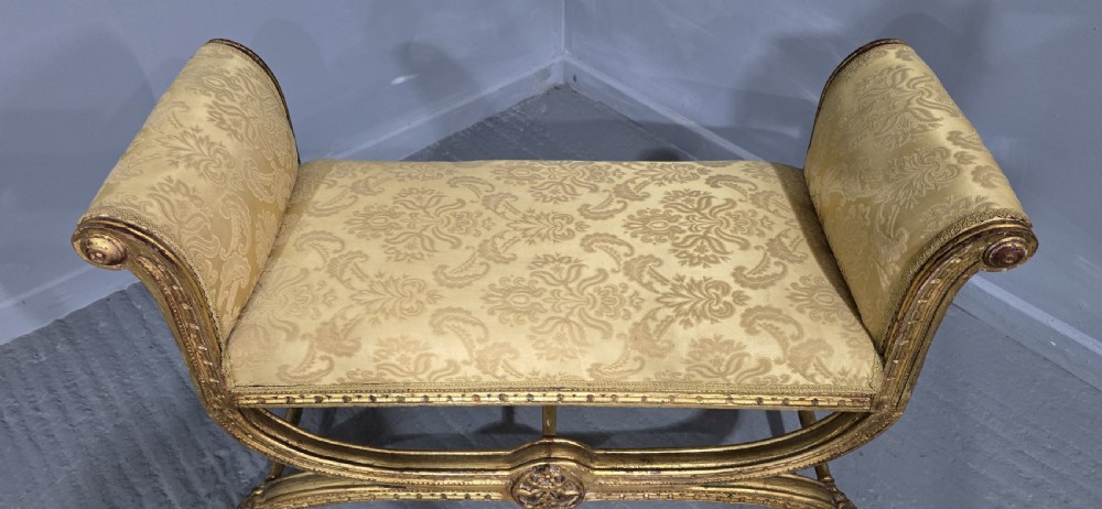 A French Neoclassical giltwood window seat featuring scrolled armrests, carved beaded frame details, and gold damask upholstery. View IV