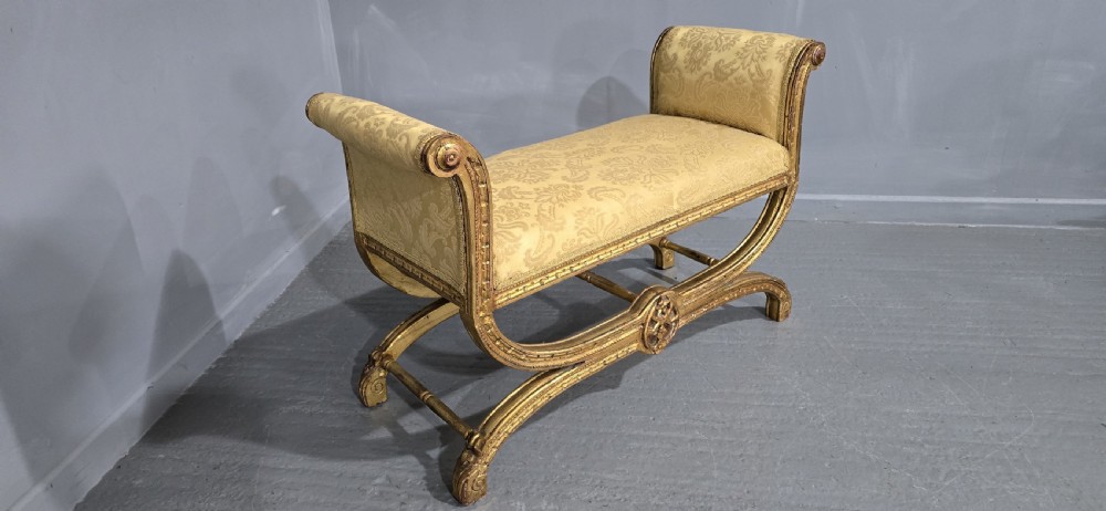 A French Neoclassical giltwood window seat featuring scrolled armrests, carved beaded frame details, and gold damask upholstery. View VI