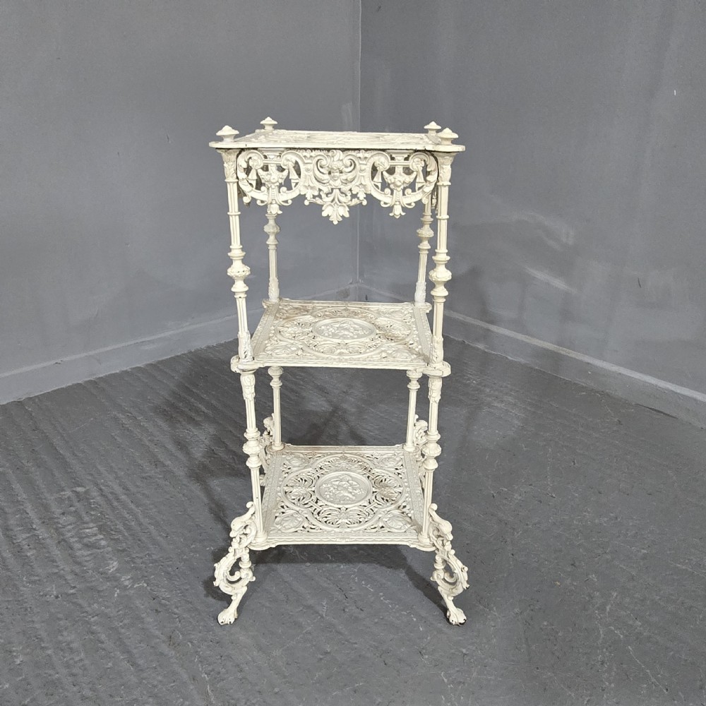 A three-tiered off-white painted cast iron jardiniere stand featuring elaborate openwork scrollwork trays, turned supports, and decorative feet.